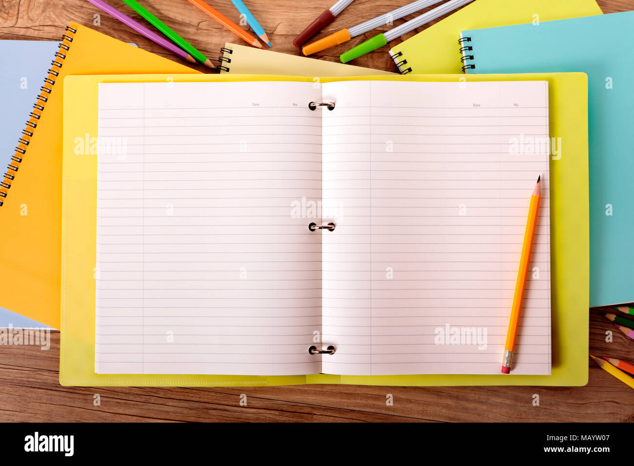 Student's desk with yellow project folder surrounded by various pens, pencils and notebooks. Stock Photo
