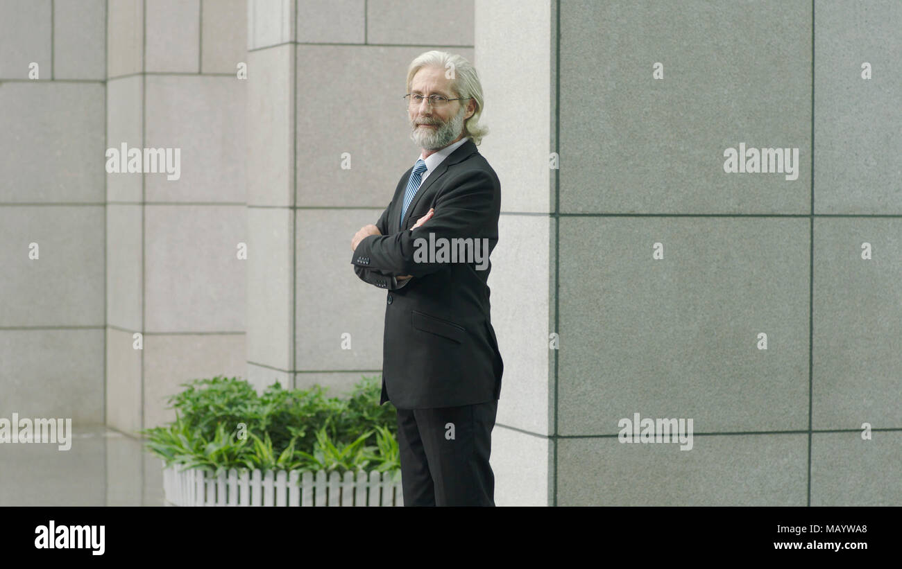 caucasian corporate executive in full suit standing in modern office building looking at camera smiling arms crossed. Stock Photo