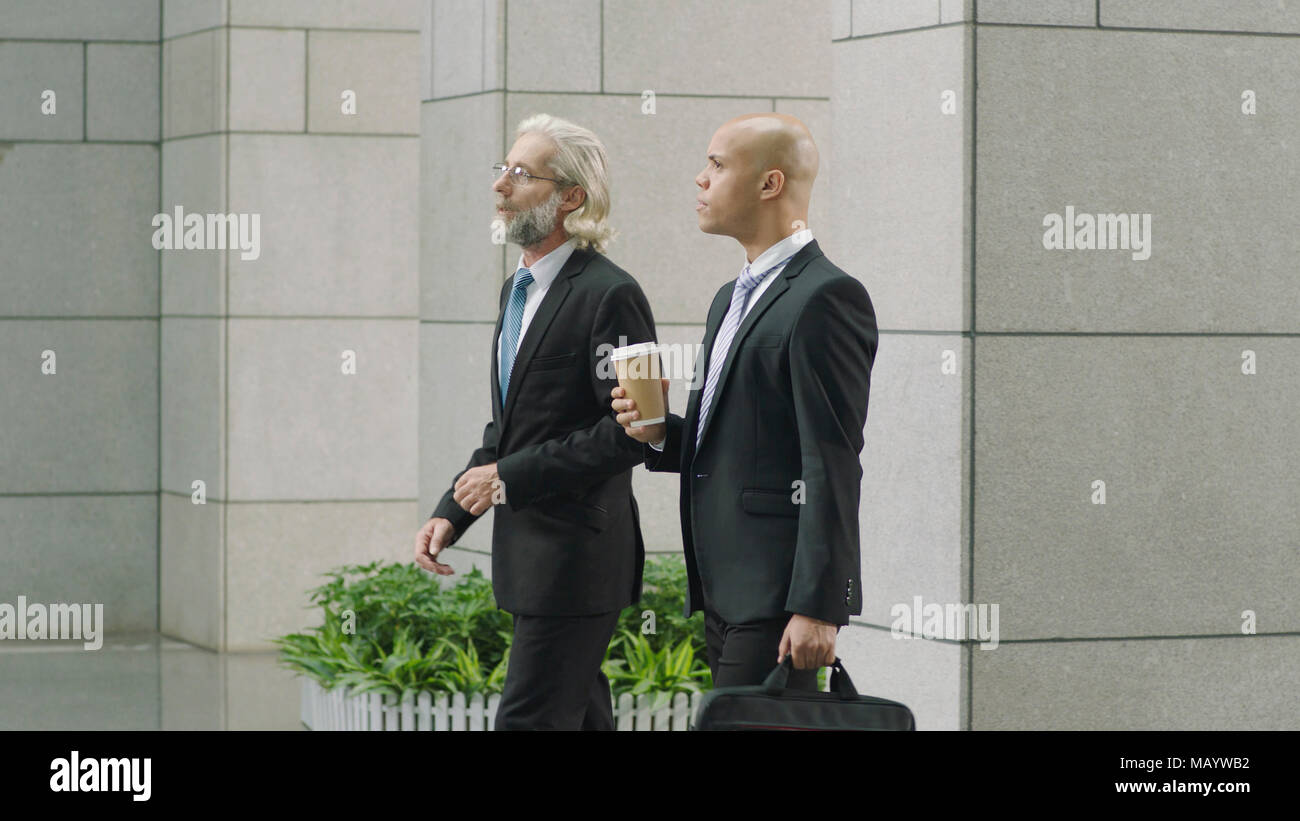 caucasian and latino corporate executives walking side by side arriving at modern office building. Stock Photo