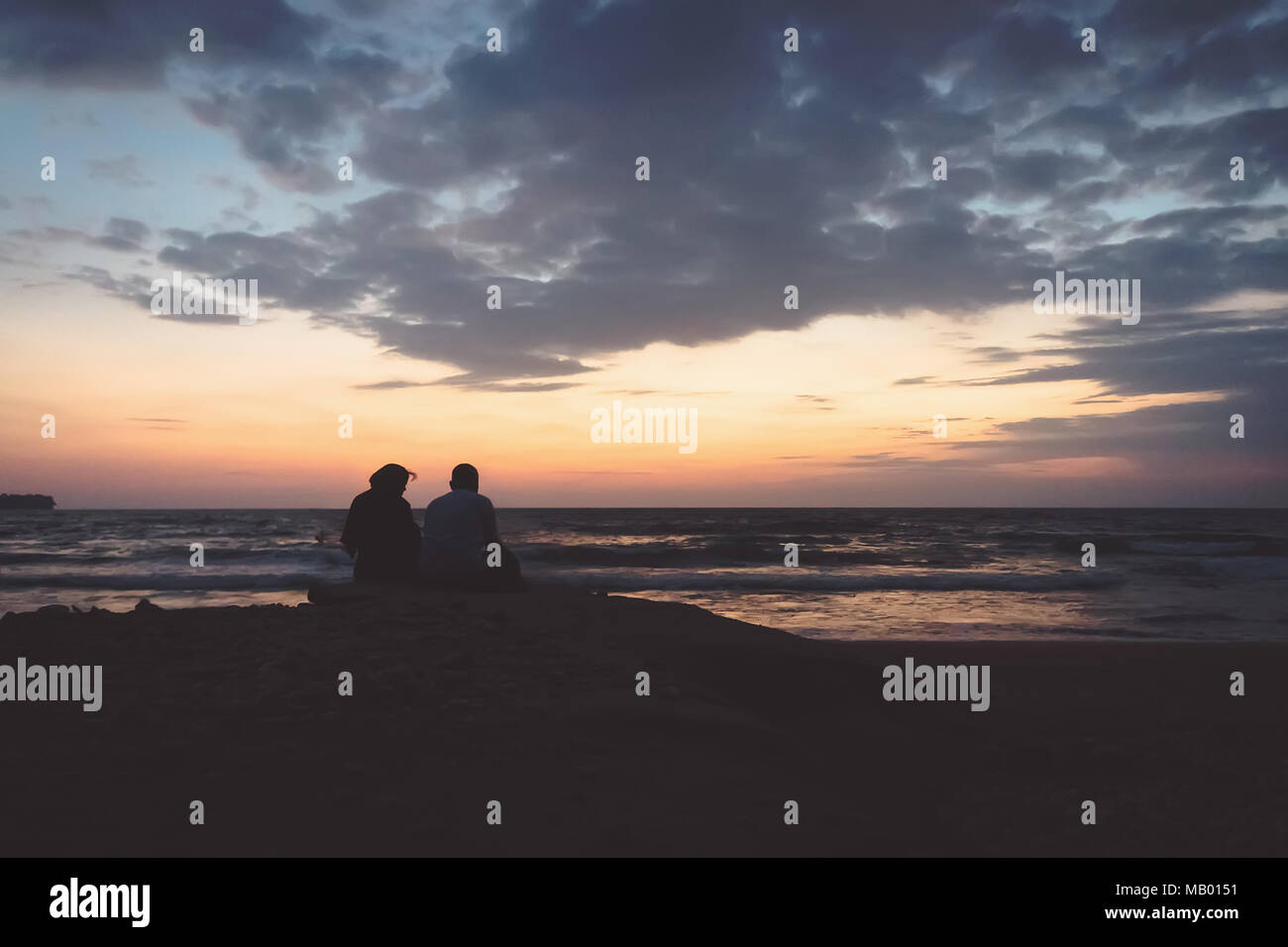 a man and a woman sit on a rock on the shore and look towards the dawn. Sunrise on the Andaman Islands India. silhouette of couple watching sunset on  Stock Photo