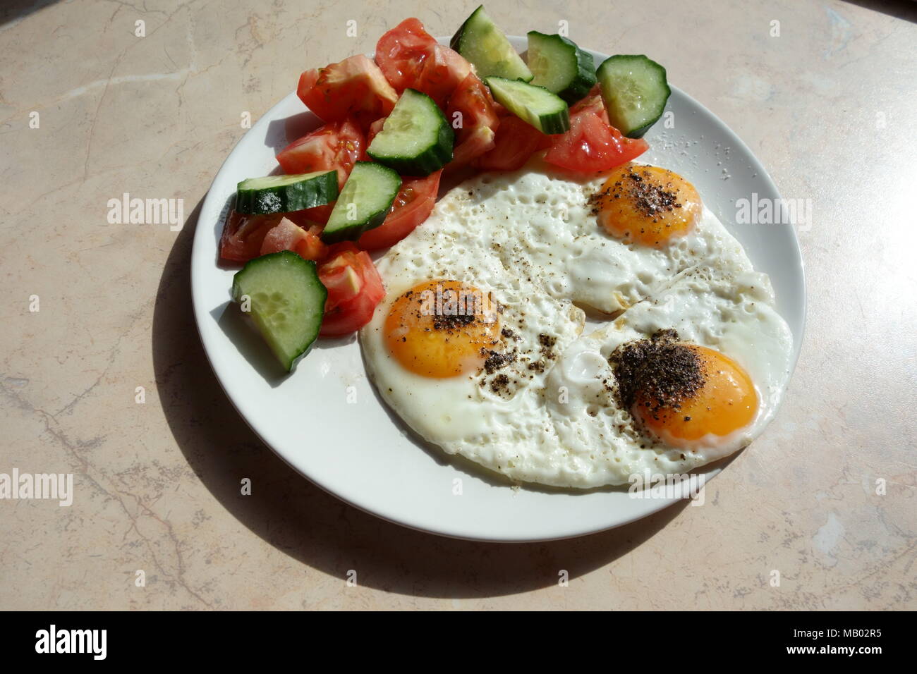 Fried eggs with raw sliced cucumber and tomato on the side Stock Photo