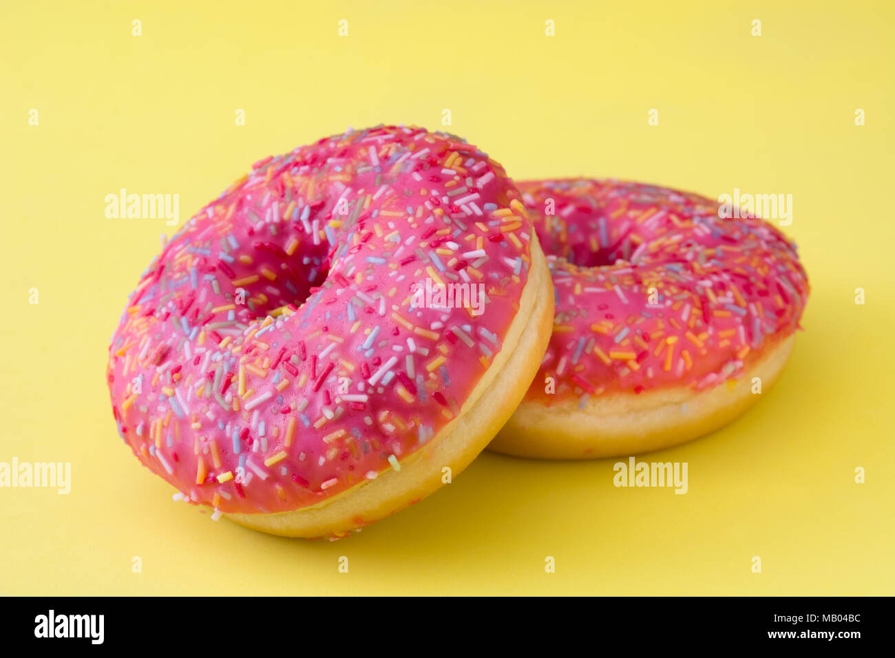 Pink frosted donut with colorful sprinkles on yellow background Stock ...