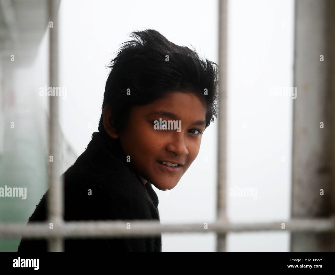 A kid from the third class of 'MV Bangali', a ferry on route from Dhaka to Morelganj seen smiling. Bangladesh is a country on water. With huge portion of its territory in the river delta of Ganga (which is called Padma here) and Brahmaputra, people have to live on water and rely on water transport. Huge ferries 'made in Bangladesh' leave river ports to transport tens of thousands of passengers every day to their destinations. Most of them just with poor - or none - radar equipment. Although many bad news about accidents, the fact is, that the river transport still remains the safest and effect Stock Photo