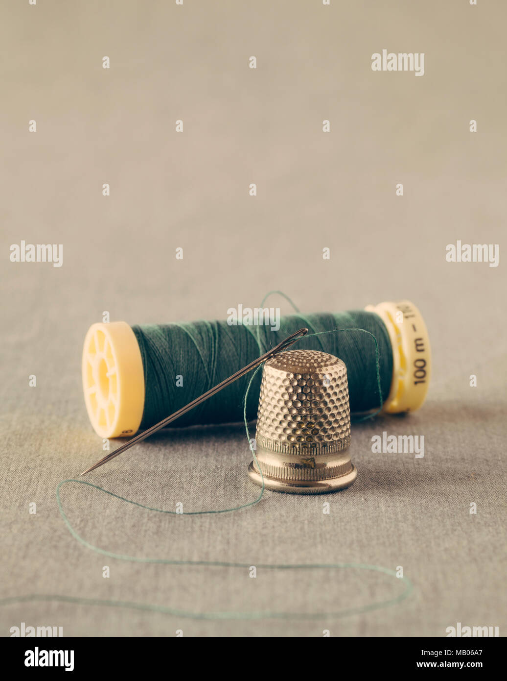 Green thread with needle and thimble close up Stock Photo