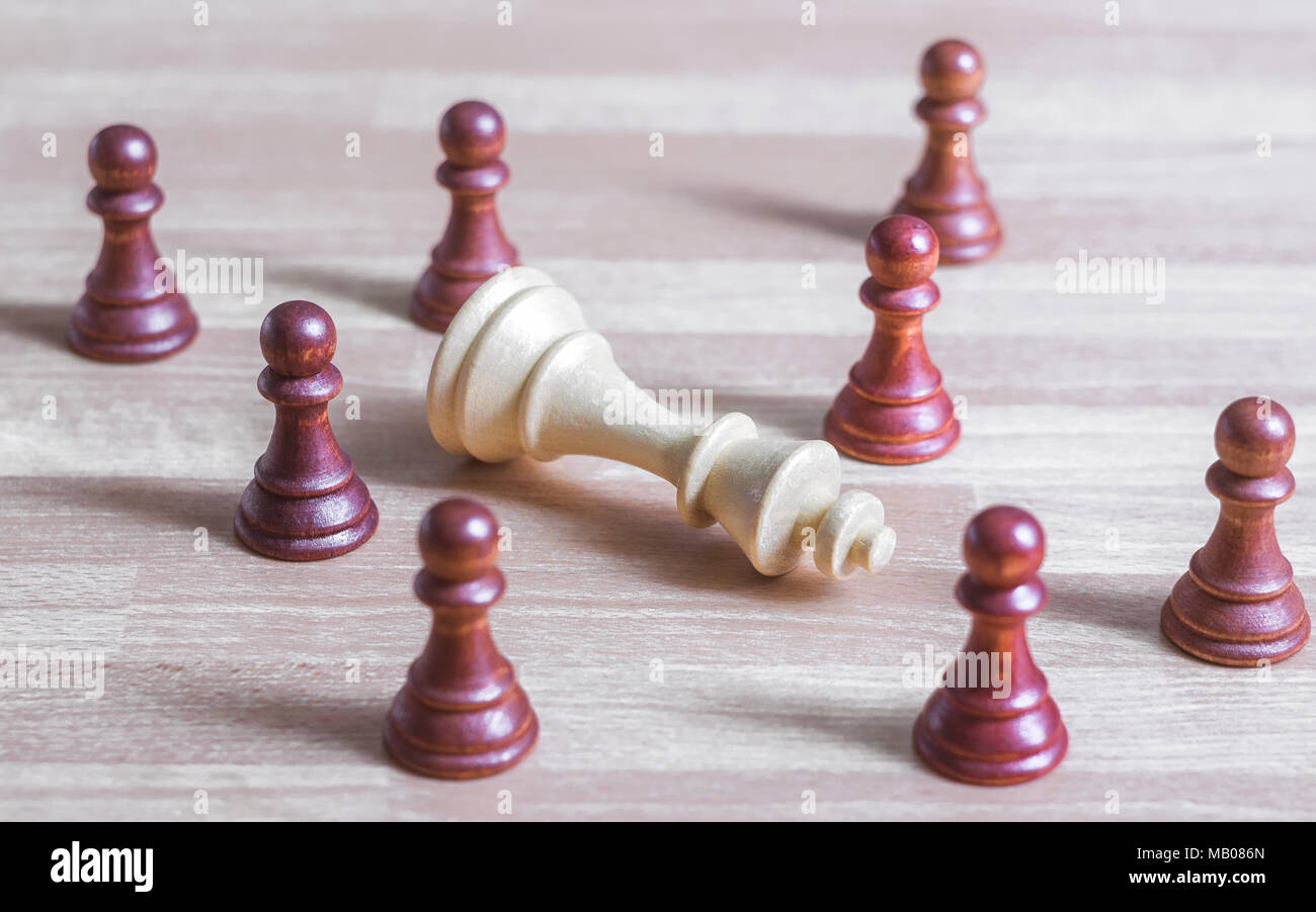 A group of black pawns looks at a dead white king chess piece Stock Photo