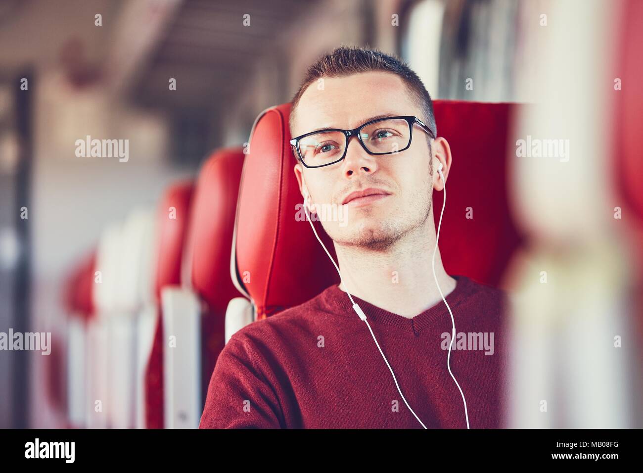 Rail transportation. Thoughtful young man with eyeglasses listening to music while traveling by train. Stock Photo