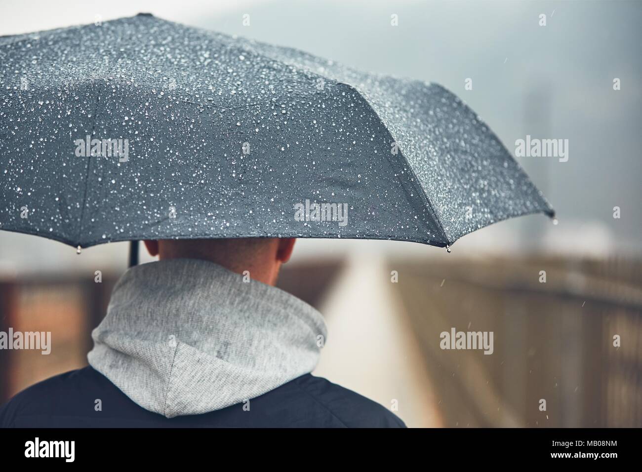 Man with umbrella in rain. Gloomy weather in city. Selective focus on the raindrop. Stock Photo