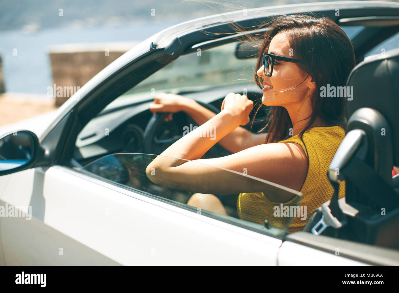 Pretty young woman with sunglasses driving in white cabriolet car