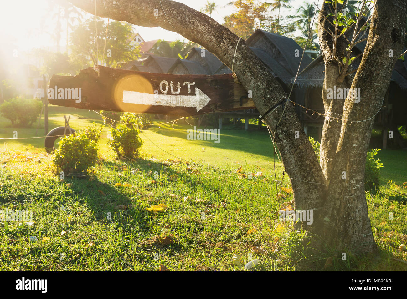 An arrow sign with the word OUT in a garden with bamboo bungolows and lens flare from sunshine in Koh Lanta, Thailand Stock Photo