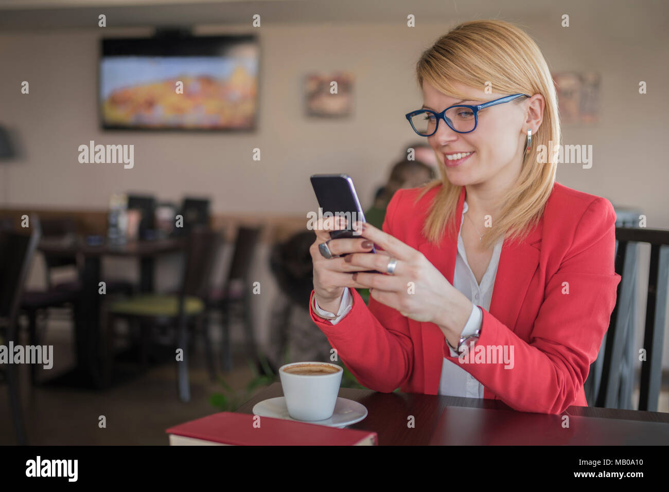 Young smiling blonde woman using smart phone, texting message in coffee ...