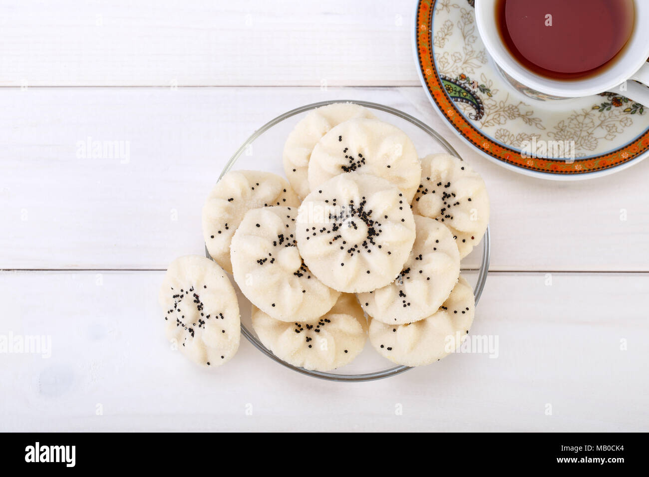 Flower Shaped Persian Sweet Rice Cookies (Naan Berenji) with Poppy Seeds and a paisley design cup and saucer tea on white wooden background Top view s Stock Photo