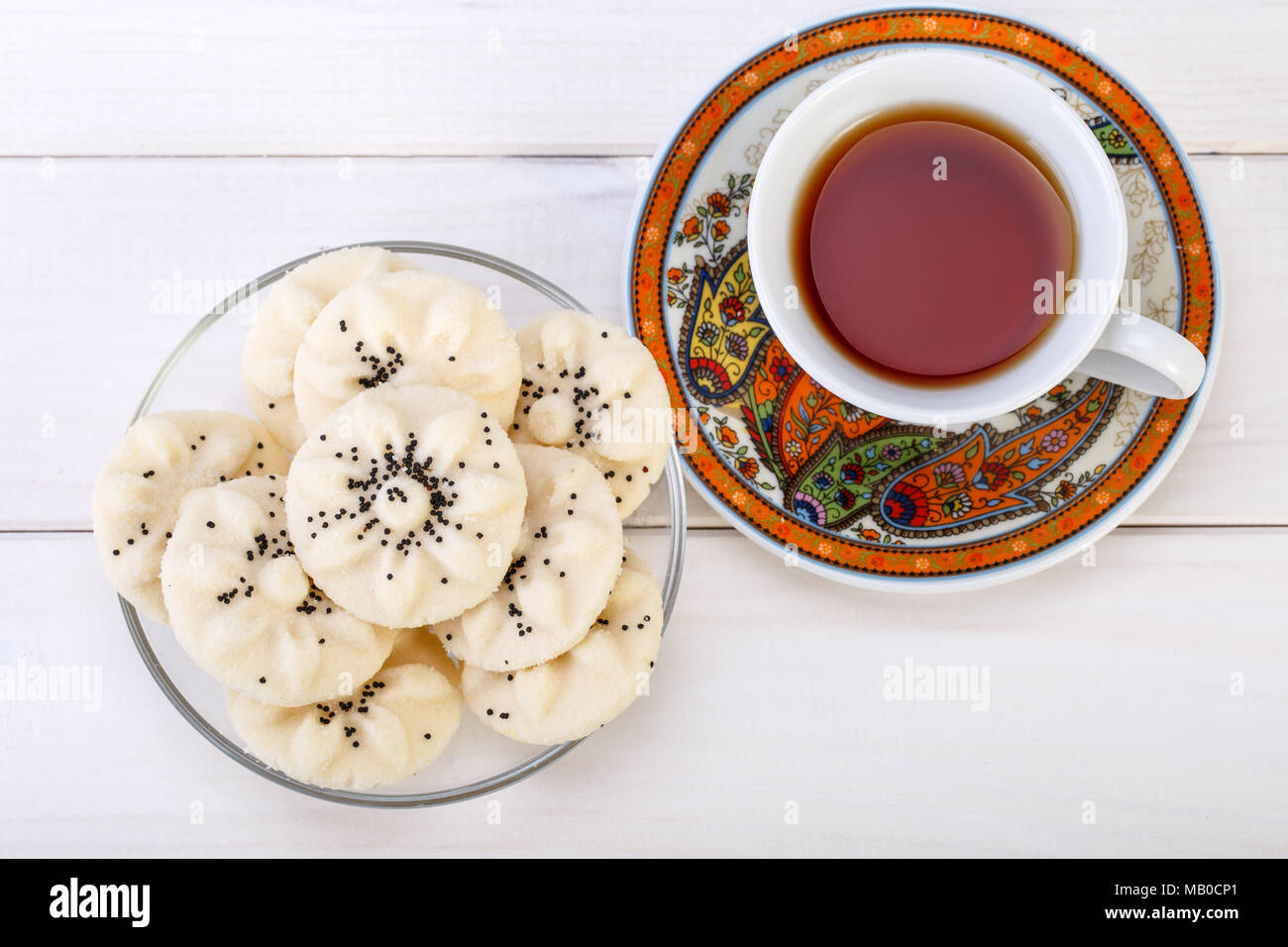 Flower Shaped Persian Sweet Rice Cookies (Naan Berenji) with Poppy Seeds and a paisley design cup and saucer tea on white wooden background Top view s Stock Photo