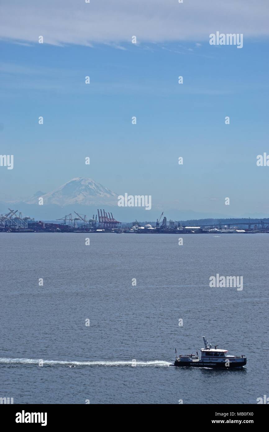 Seattle, Washington: Seattle Fire Department boat races across Elliott Bay, as snow-capped Mount Ranier seems to float in mid-air in the distance. Stock Photo