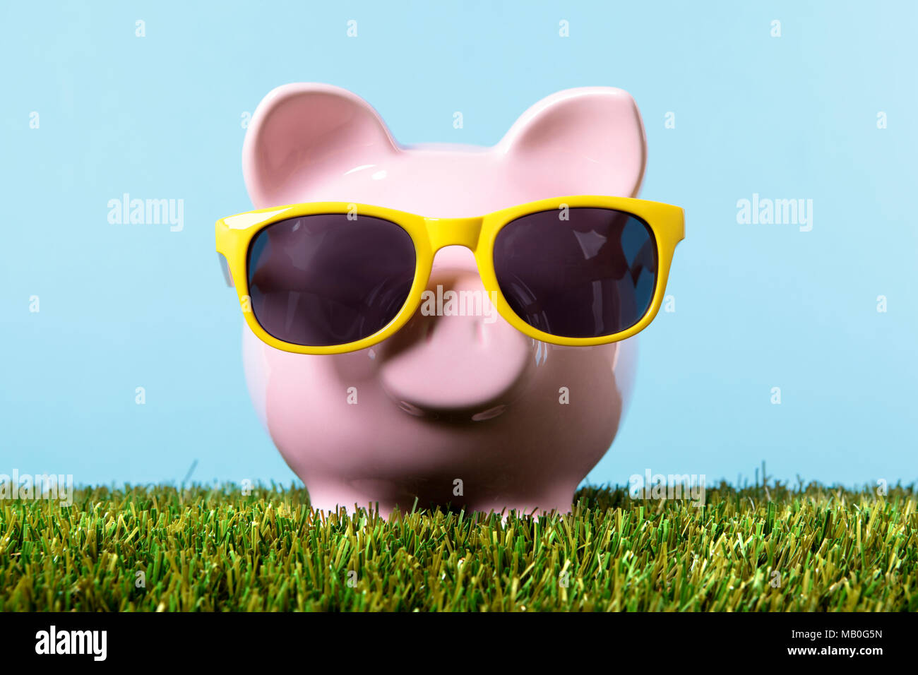Piggy bank on summer vacation with yellow sunglasses and green field Stock Photo