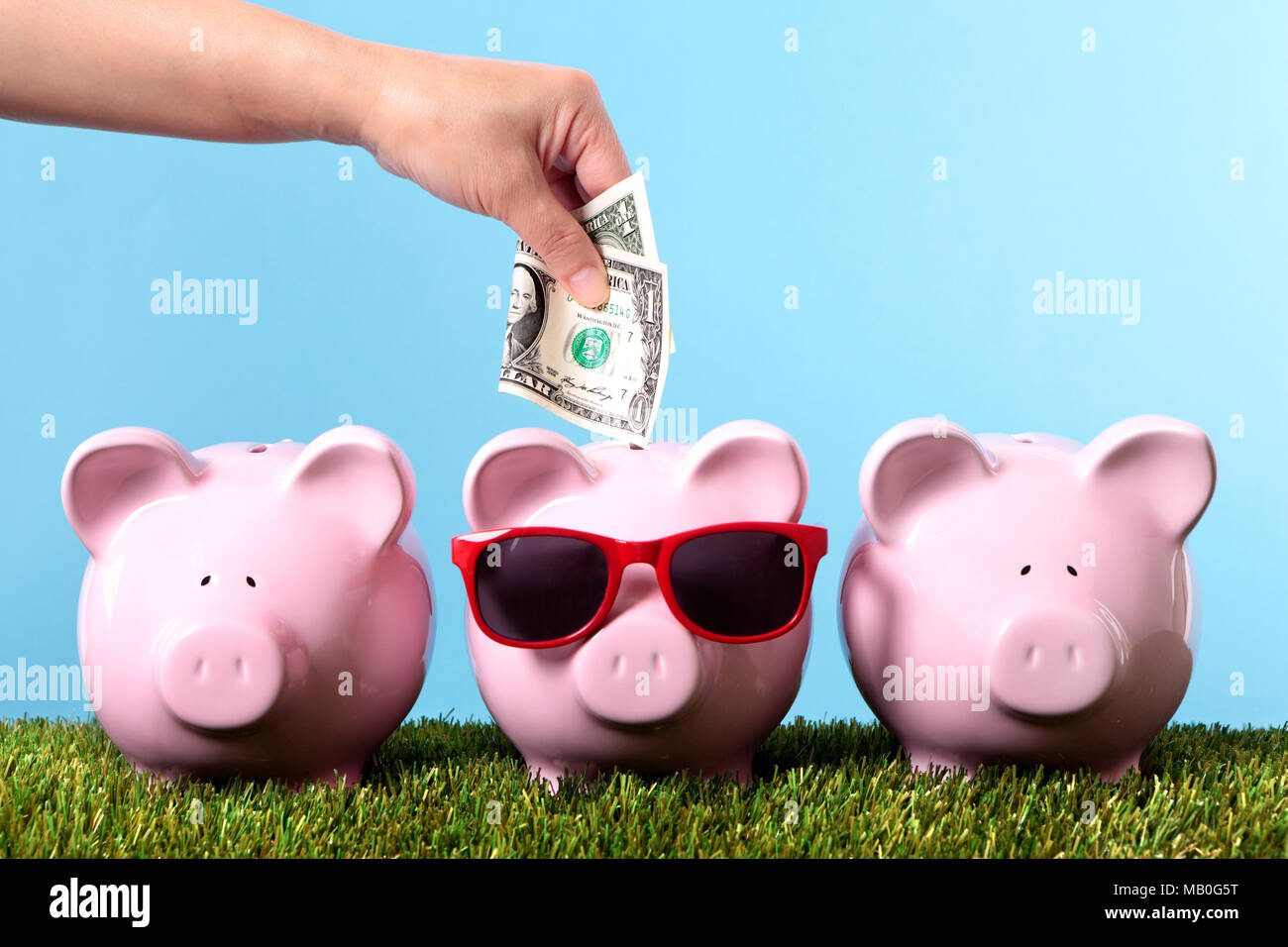 Female hand putting a one dollar bill into a pink piggy bank wearing sunglasses Stock Photo