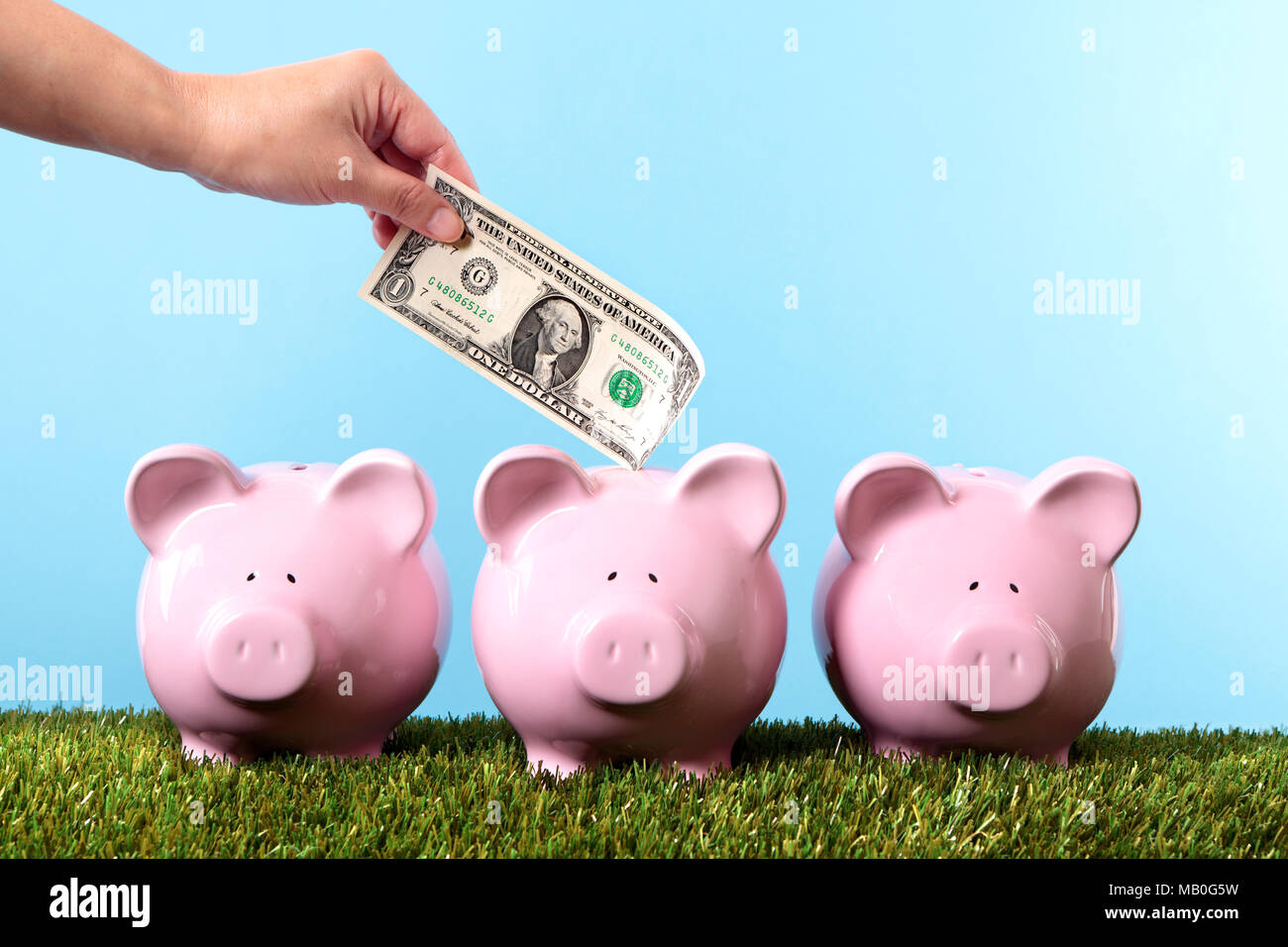 Female hand putting a one dollar bill into a pink piggy bank Stock Photo