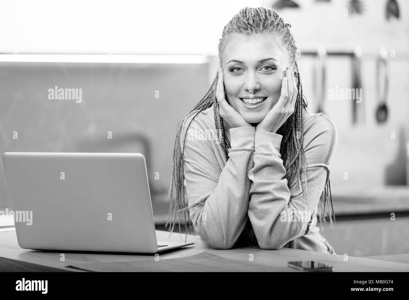 Young cheerful long-haired woman with box braids sitting next to laptop Stock Photo