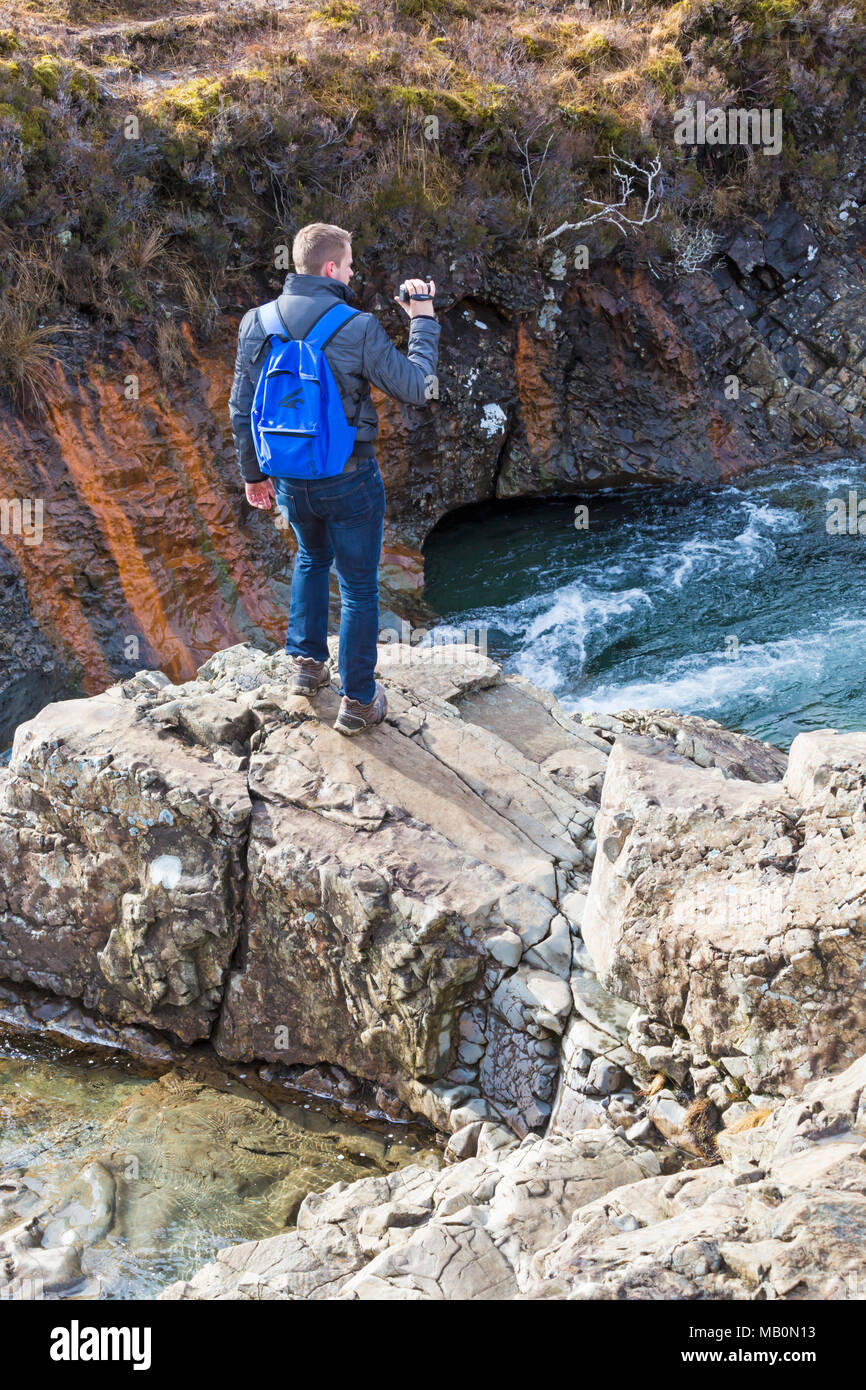 Man standing on rocks holding panasonic video camera to capture the scenery at Fairy Pools, river Brittle, Isle of Skye, Scotland, UK in March Stock Photo