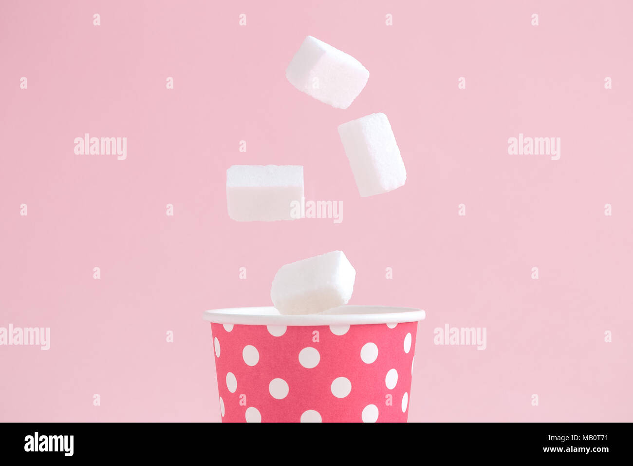 Sugar cubes falling into paper cup polka design against pastel pink ...