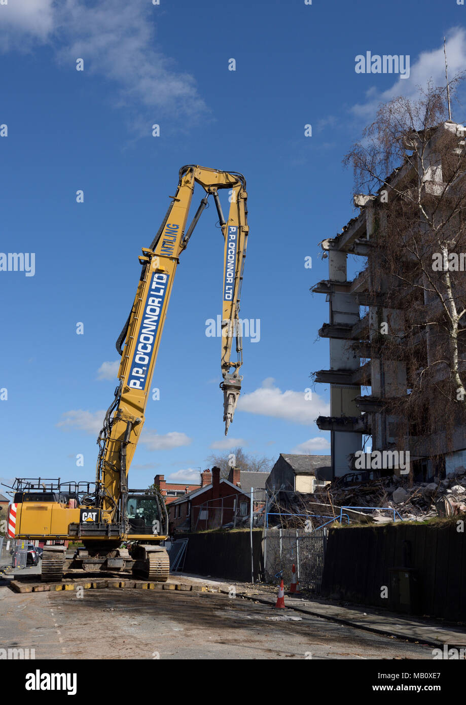 Caterpillar 350L high reach demolition excavator with concrete crusher attachment on road in front of partly demolished concrete building in bury uk Stock Photo