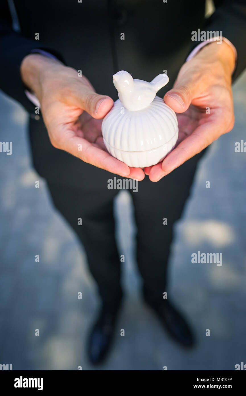 A man in black suit holding white ceramic box with a bird Stock Photo