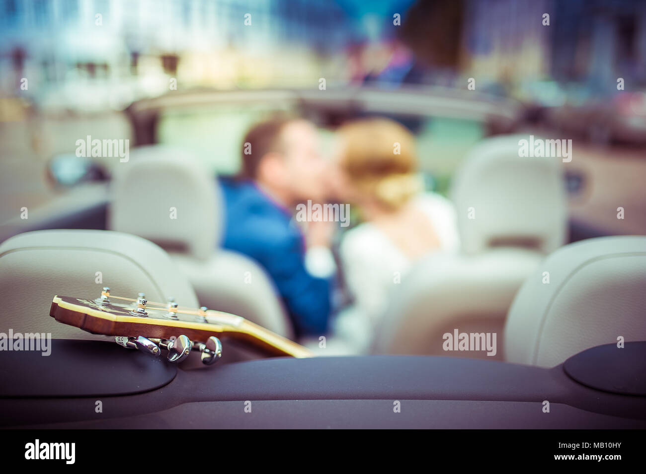 Kissing couple in a cabriolet with a guitar in the back Stock Photo