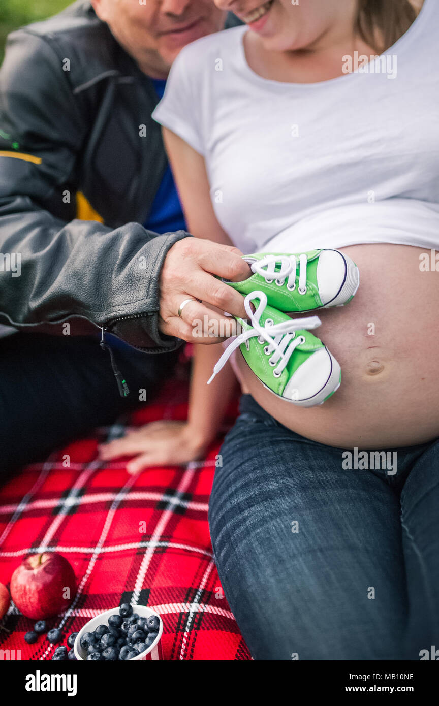 Pregnant couple picnicking while waiting for a baby. Green baby sneakers waiting for their owner on mother's belly Stock Photo