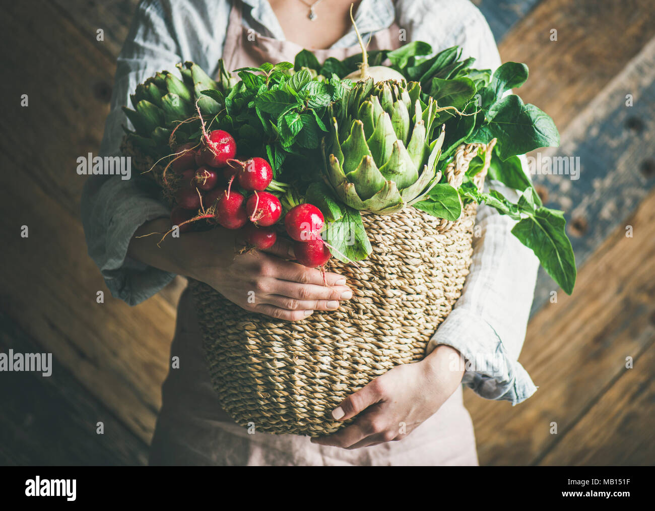 Female farmer in linen apron holding basket of fresh garden vegetables ...