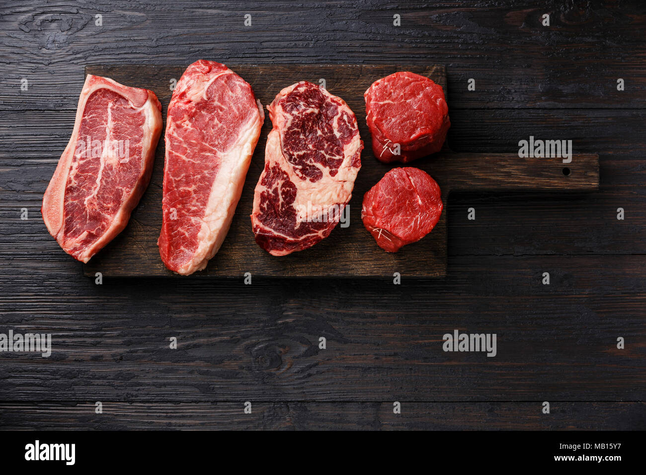 Variety of Raw Black Angus Prime meat steaks Blade on bone, Striploin, Rib eye, Tenderloin fillet mignon on wooden board copy space Stock Photo