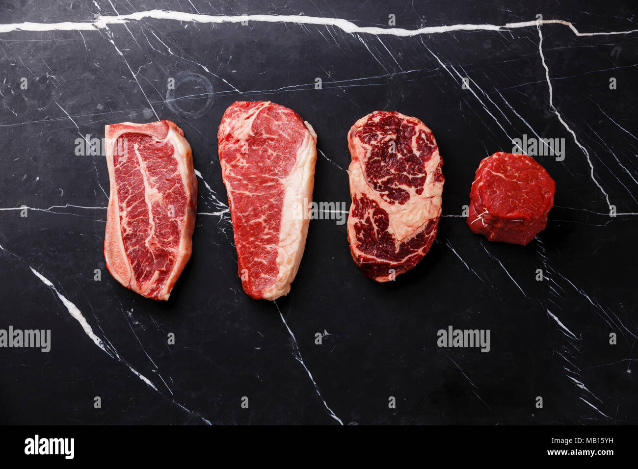 Variety of Raw Black Angus Prime meat steaks Blade on bone, Striploin, Rib eye, Tenderloin fillet mignon on dark marble background copy space Stock Photo