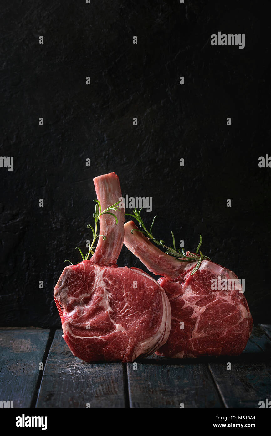 Raw uncooked black angus beef tomahawk steaks on bones served with rosemary over dark wooden plank table. Rustic style. Close up Stock Photo