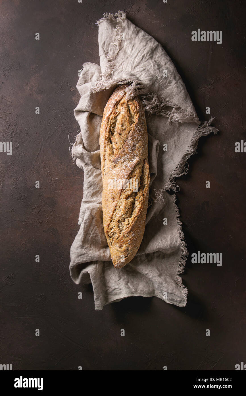 Loaf of fresh baked artisan rye bread on linen cloth over dark brown ...