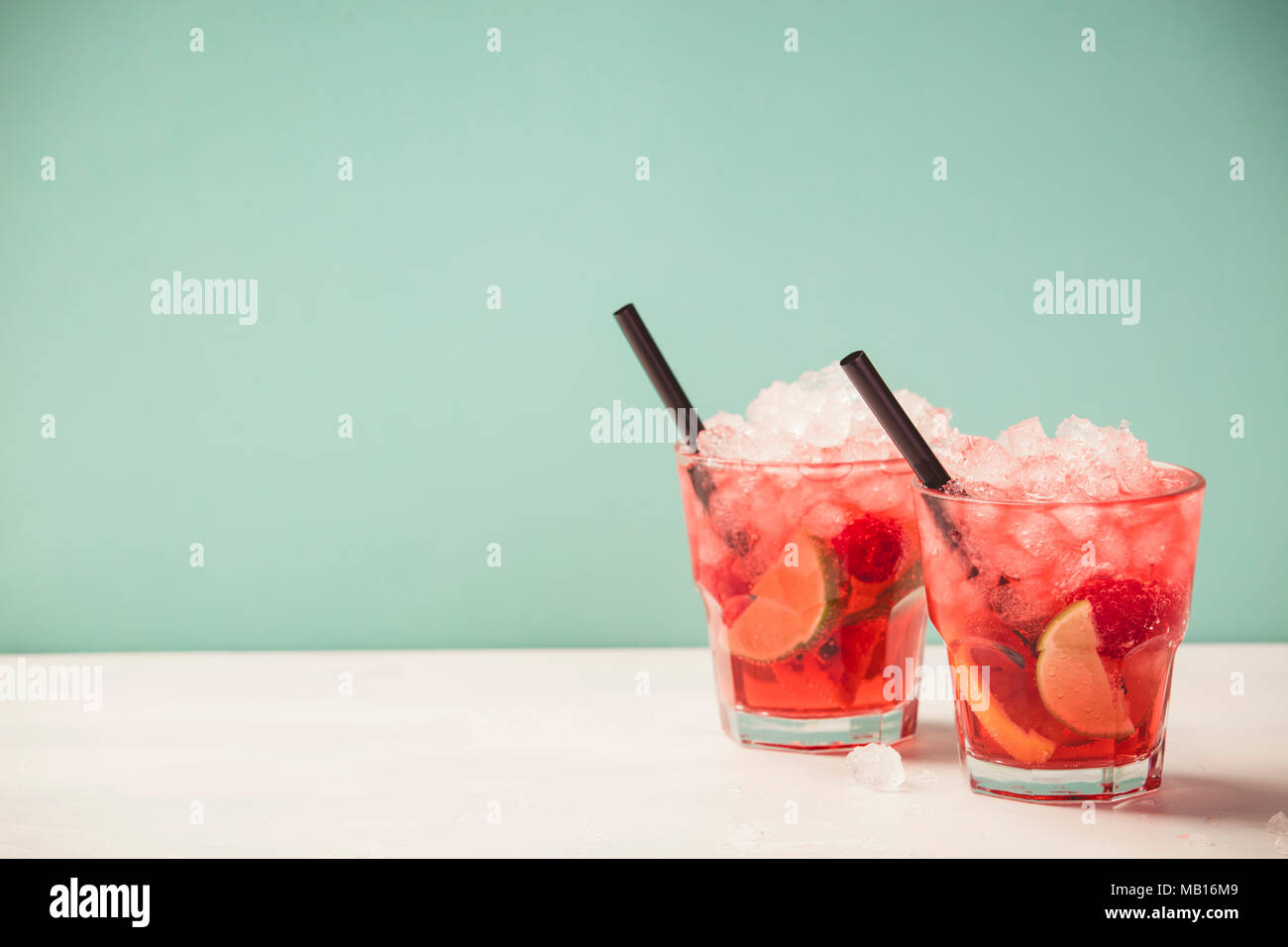 Red drink with ice. Cocktail making bar tools, raspberry, lime, oranges and mint leaves. Raspberry mojito on blue background Stock Photo