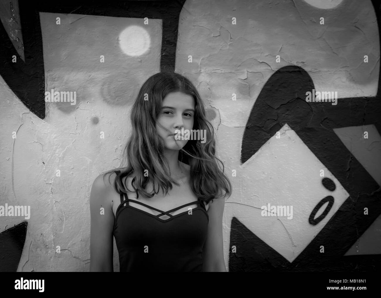 Pretty, serious teen girl portrait, long hair, grunge background, black and white. Beautiful Caucasian teenage girl in summer top, flowing hair. Stock Photo