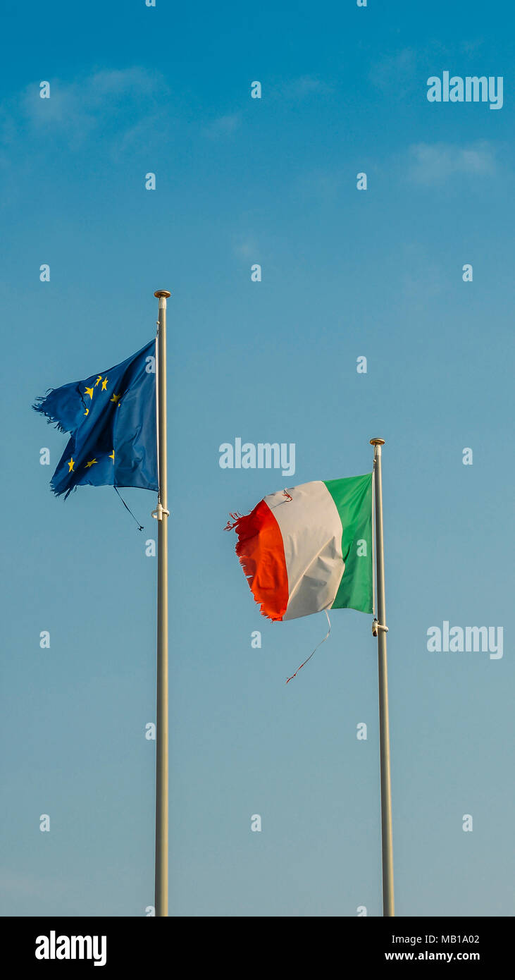 Italy flag and Europe flag waving together on a mast in isolated the blue sky background. Concept for financial treated, unique currency and financial bond despite the torn sides. Stock Photo