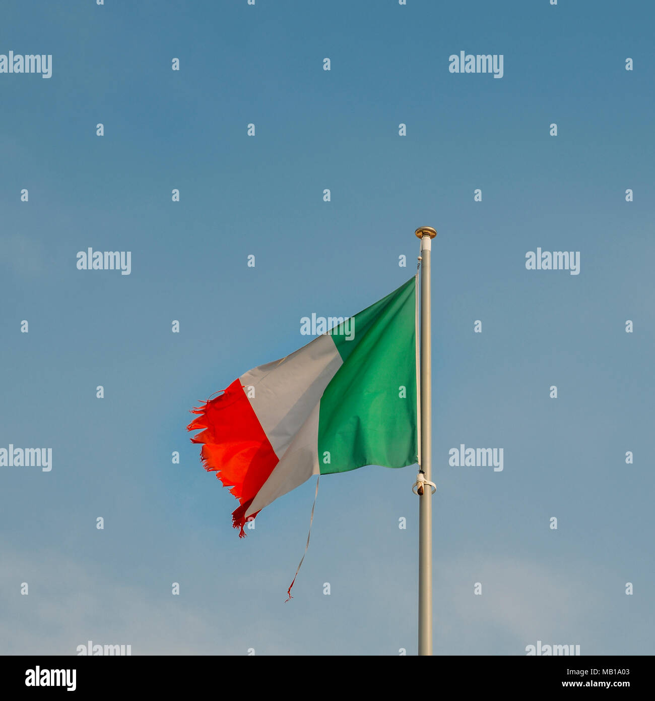 Italian flag on the mast blowing in the wind with ripped corners, perhaps a metaphor for a series of political and economic crisis facing the country. Stock Photo