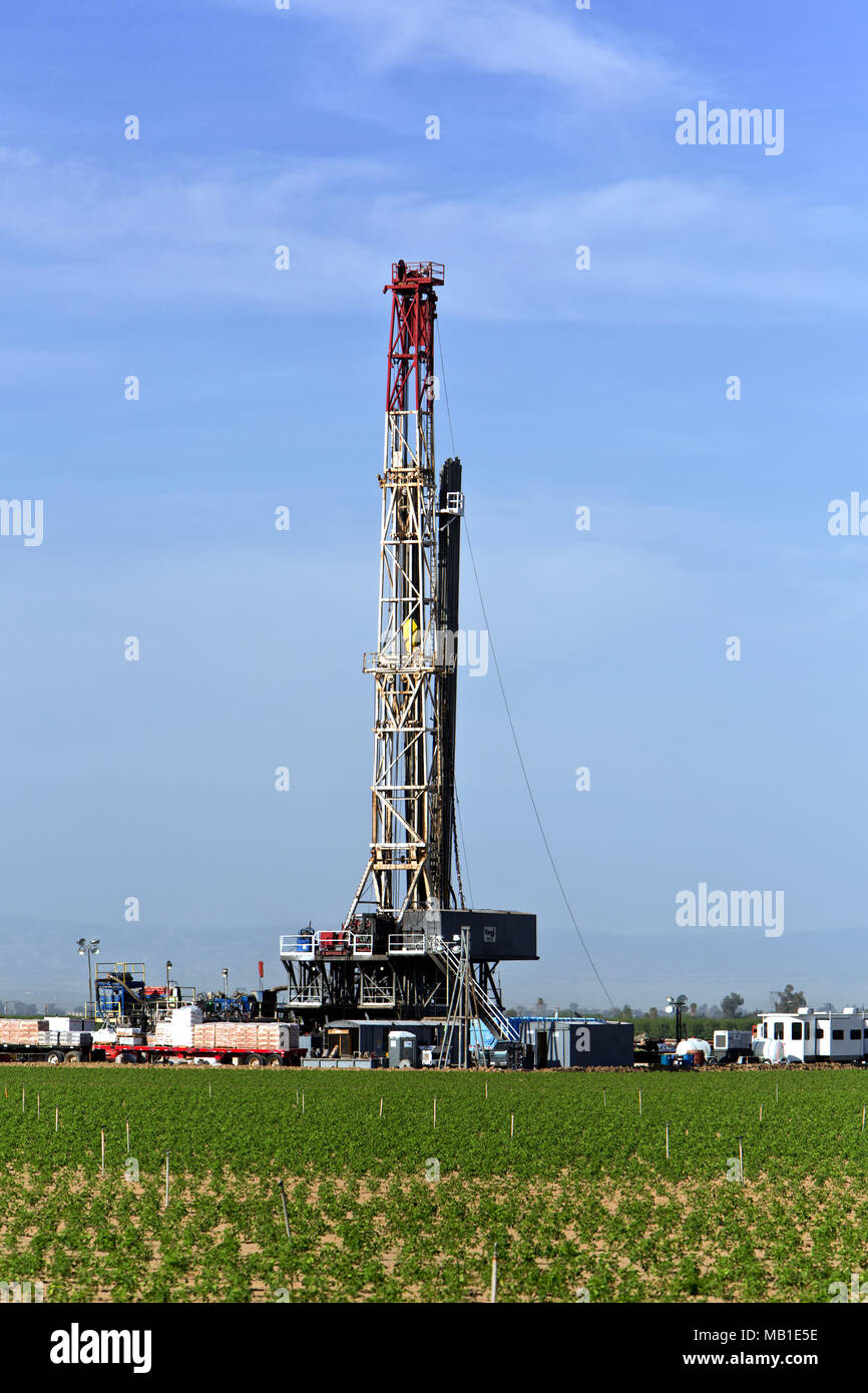 Drilling rig operating in productive tomato field in foreground,  oil exploration, morning light, Kern County. Stock Photo