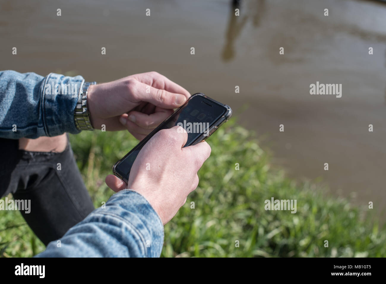 Young Person Looking At Their Mobile Phone On The Bank Of The