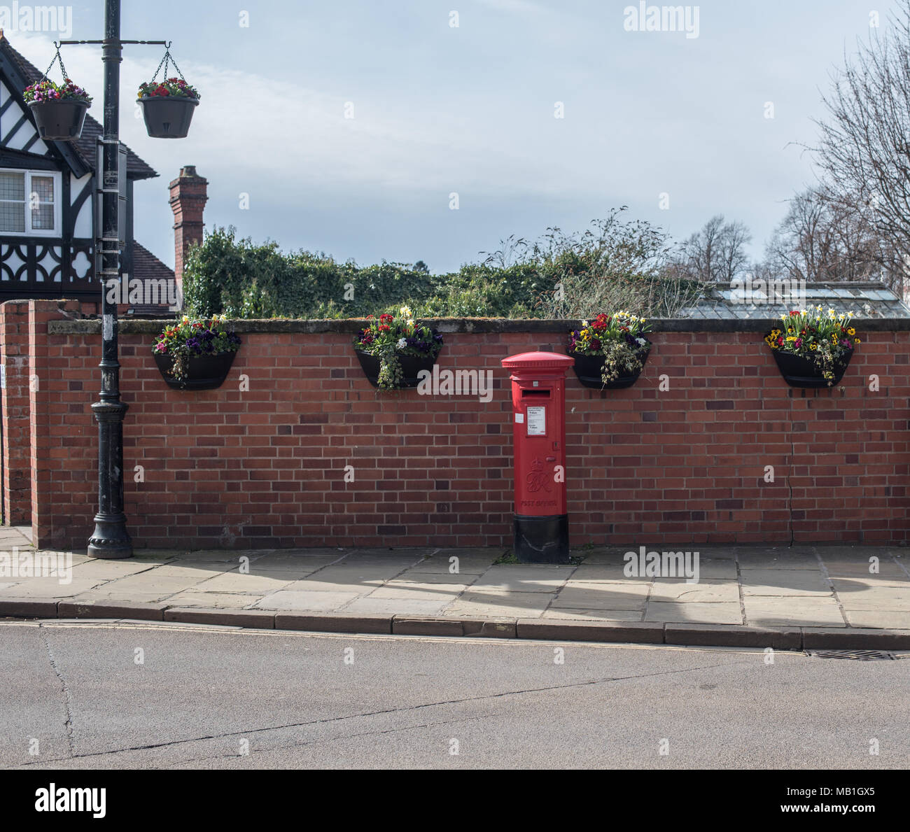 Urban classic red post box against a red brick wall and flower baskets
