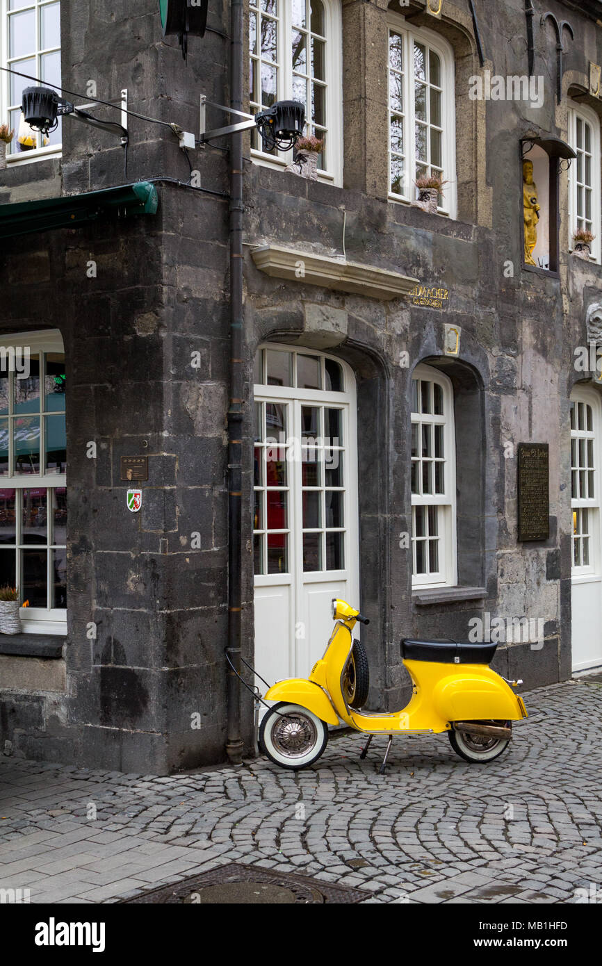 A yellow old model scooter locked to a rain pipe  of a historic house in the center of the german city of Essen. Stock Photo