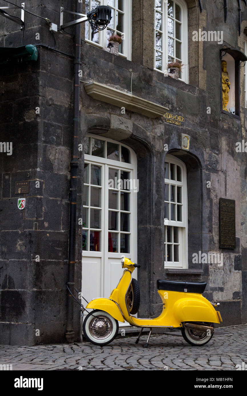 A yellow old model scooter locked to a rain pipe  of a historic house in the center of the german city of Essen. Stock Photo