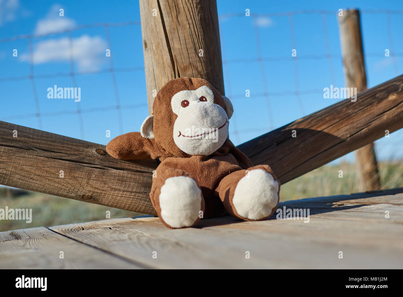 Closeup of a lovely brown and white toy monkey smiling happily sitting on a wooden floor and leaning comfortably on a wooden railing Stock Photo