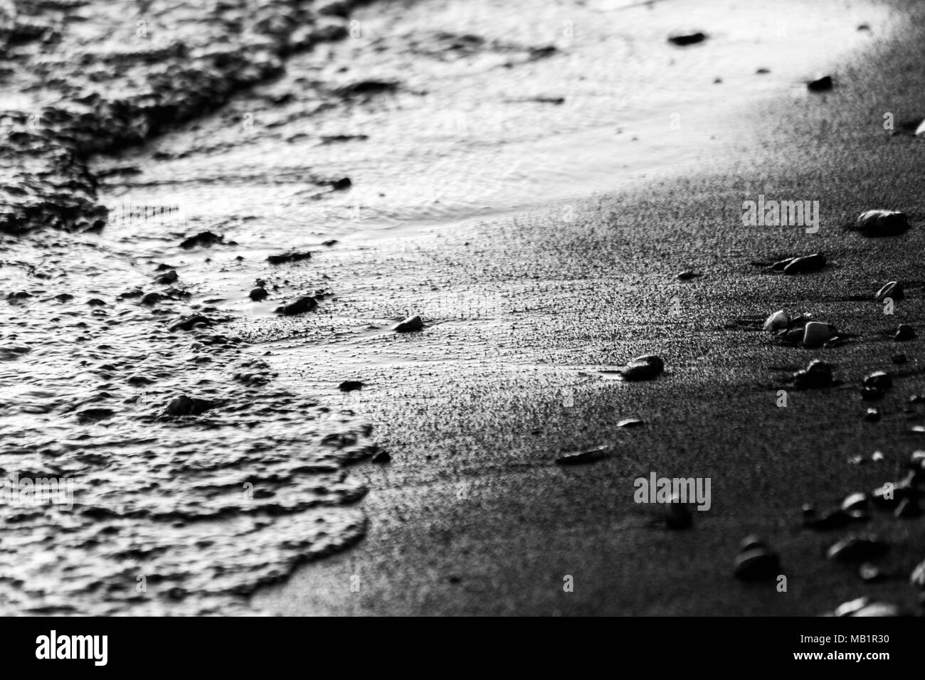 A close view of water on a lake shore at sunset, with details of sands and little round stones Stock Photo