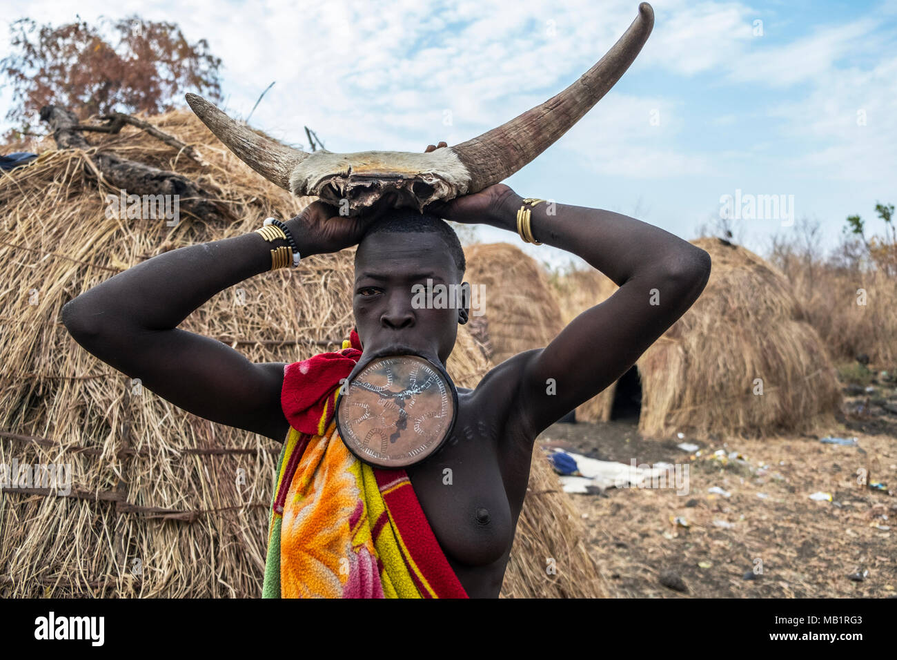 OMORATE, ETHIOPIA - JANUARY 24, 2018: Woman of the Mursi tribe with traditional jewelry with the typical houses of the Mursi in Ethiopia. Stock Photo