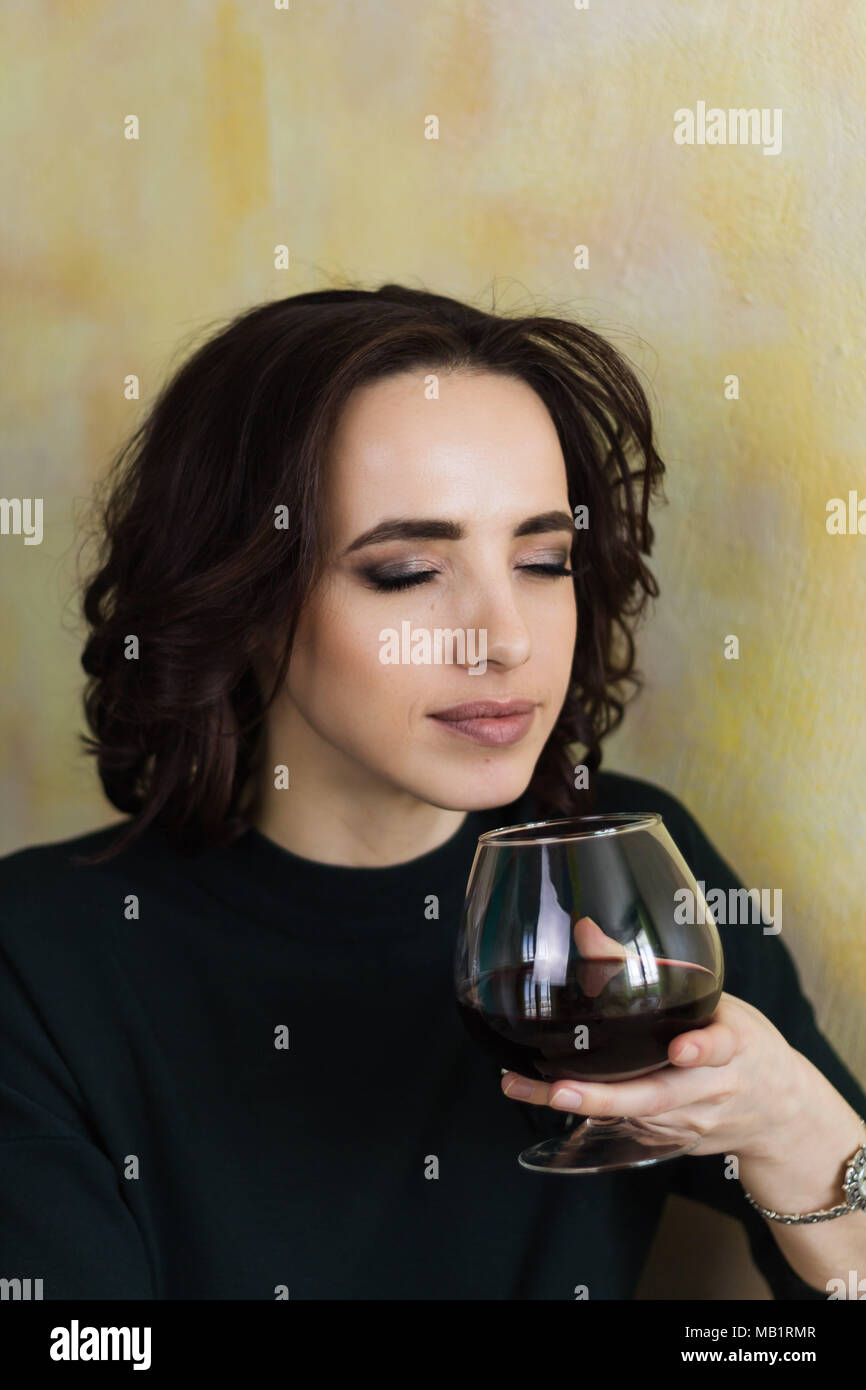 beautiful woman with closed eyes holds a glass of red wine and inhales its aroma Stock Photo