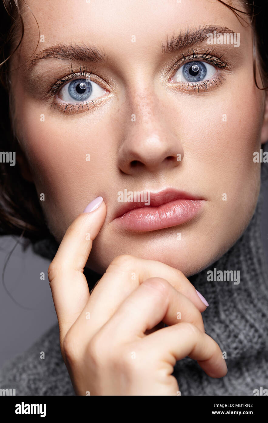Beauty portrait of young woman in gray wool sweater. Brunette girl with bright blue eyes and day female makeup. Stock Photo