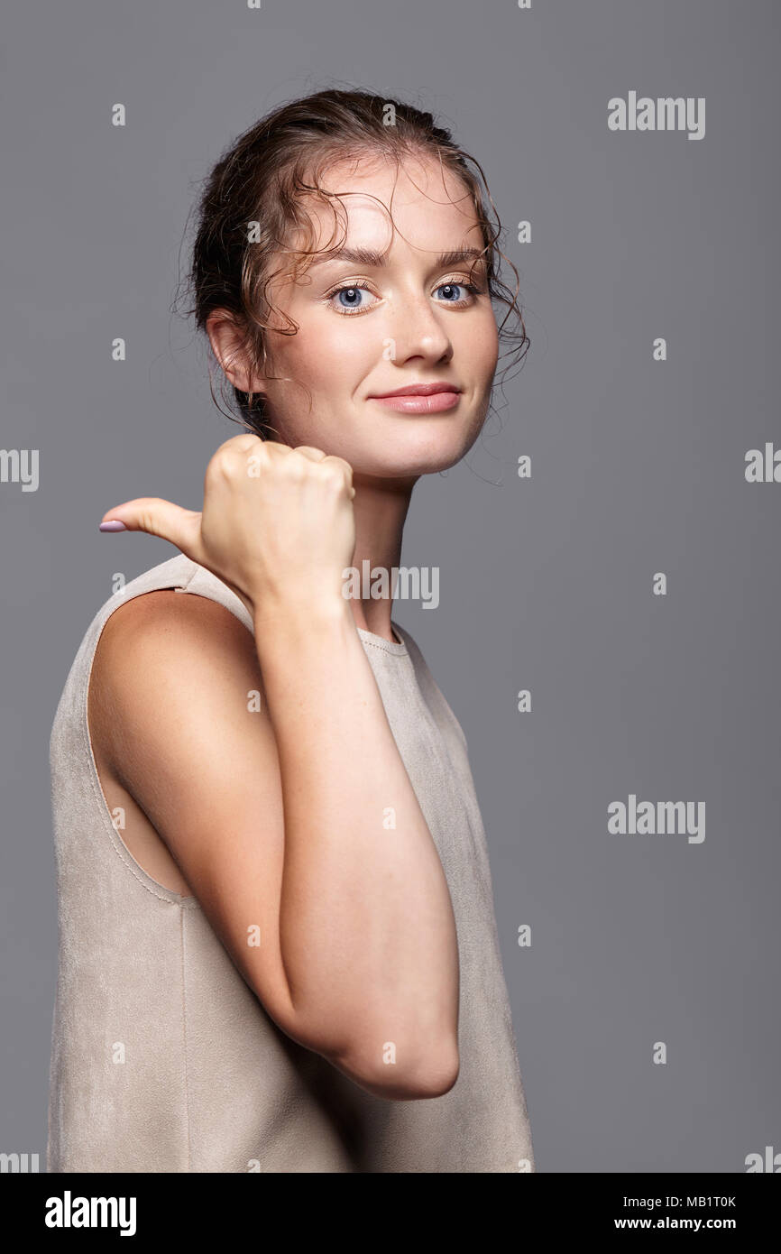 Beautiful woman smiling and pointing at copy space. Young female in casual dress on gray background Stock Photo