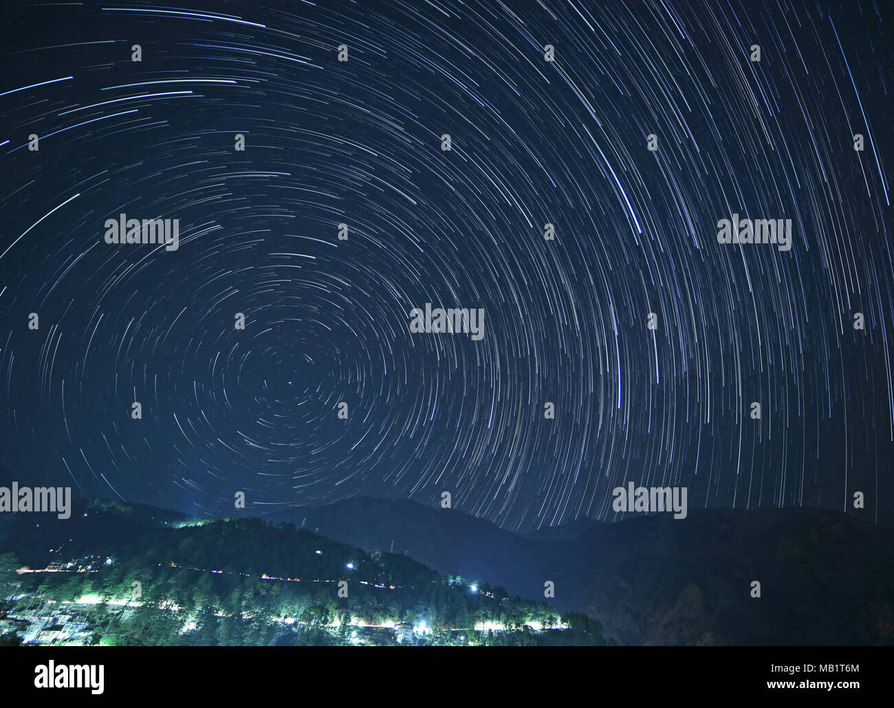 McLeod Ganj at night with star trails in sky above mountains, India Stock Photo