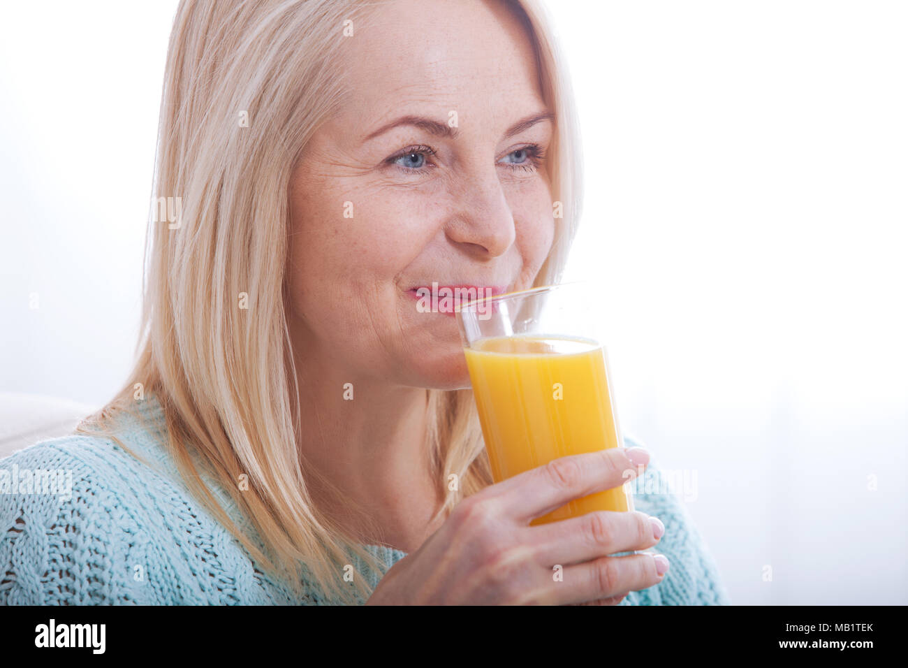 Woman drinking orange juice smiling. Beautiful middle aged Caucasian model face closeup. Stock Photo