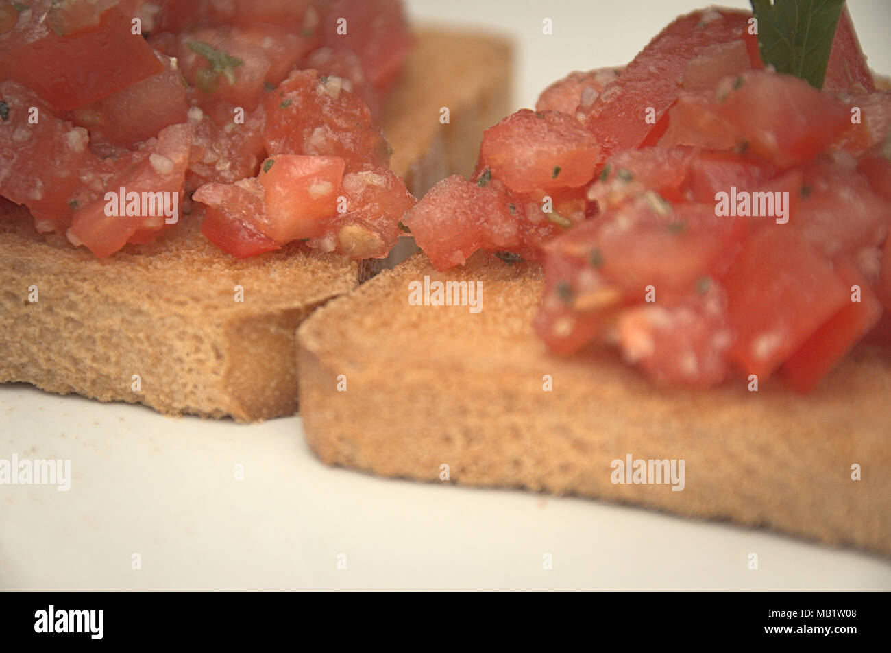 Bruschetta, toast bread with tomato and garlic, pepper, spices and something green on top. Crisp and tasty Mediterranean food. Stock Photo